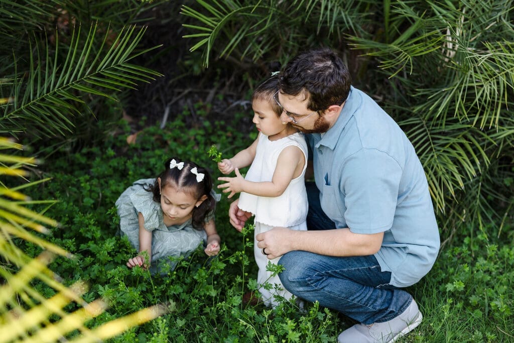 Dad kneeling with his two young daughters during a family photo session at Manistee Ranch Park in Glendale, Arizona.