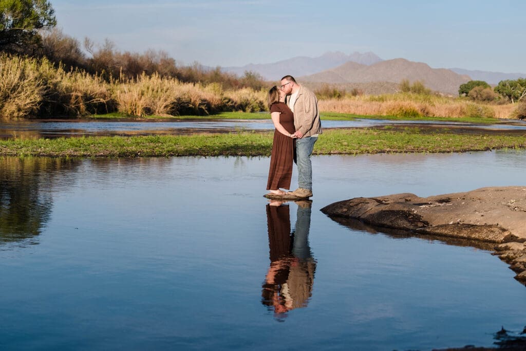 Couple kissing during Salt River engagement photos with their reflection in the water