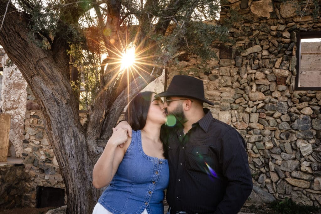 Engaged couple kissing at Scorpion Gulch with sunlight coming through the trees and historic stone walls at South Mountain in Phoenix, Arizona.