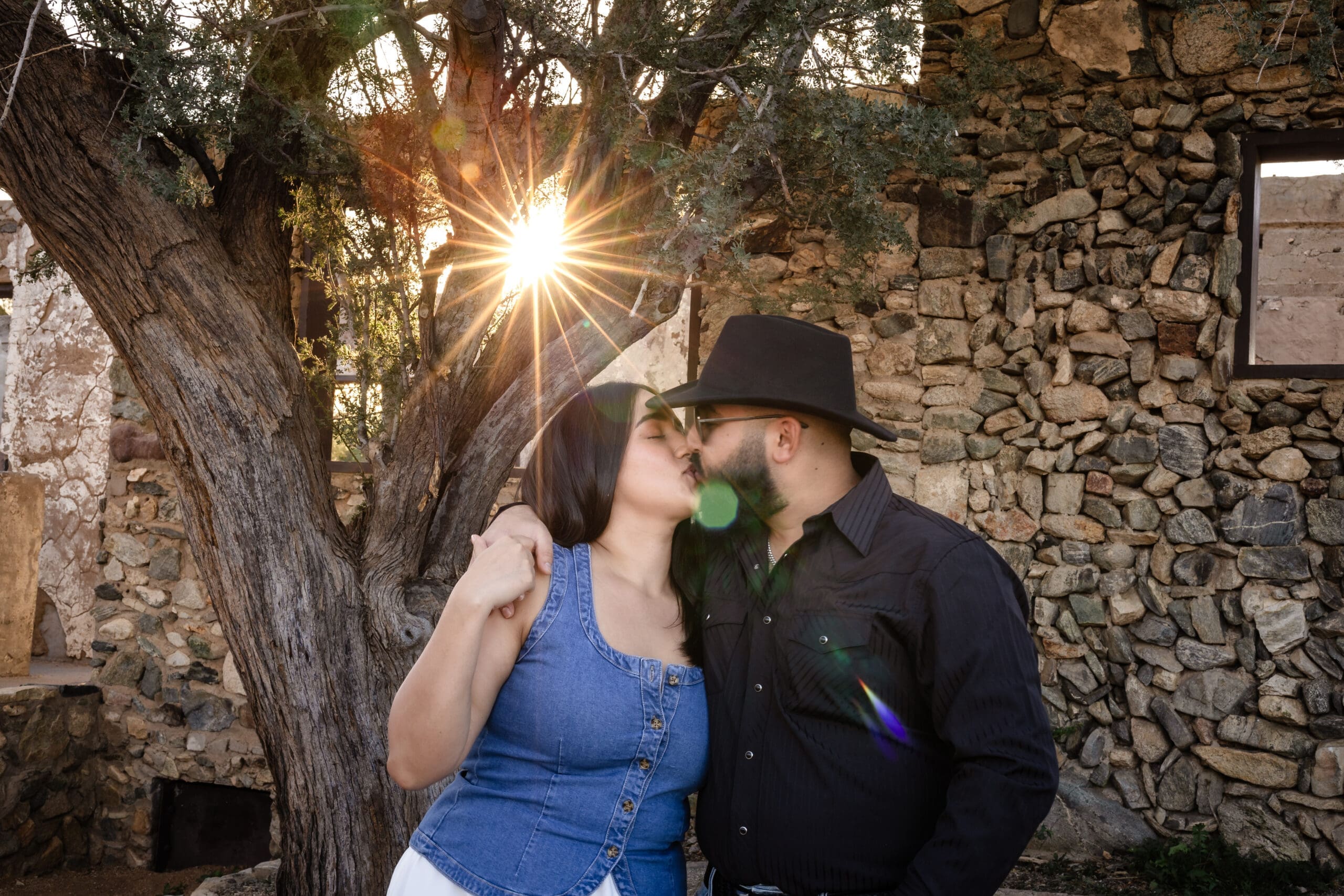 Engaged couple kissing at Scorpion Gulch with sunlight coming through the trees and historic stone walls at South Mountain in Phoenix, Arizona.