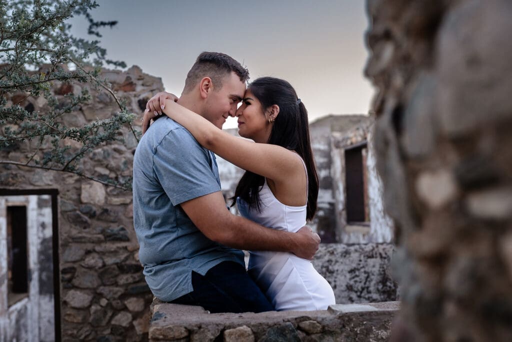 Engaged couple sitting close together at Scorpion Gulch with historic stone walls during a photo session in Phoenix, Arizona.