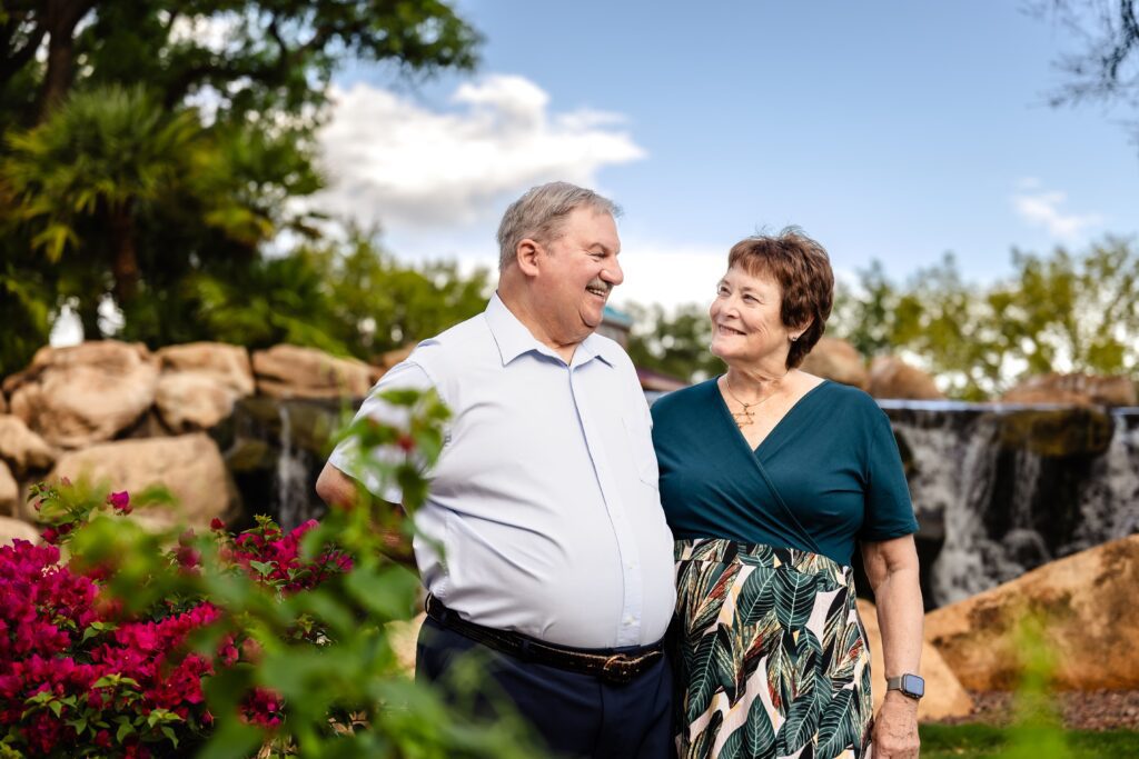 Older husband and wife standing beside pink flowers at Anthem Community Park