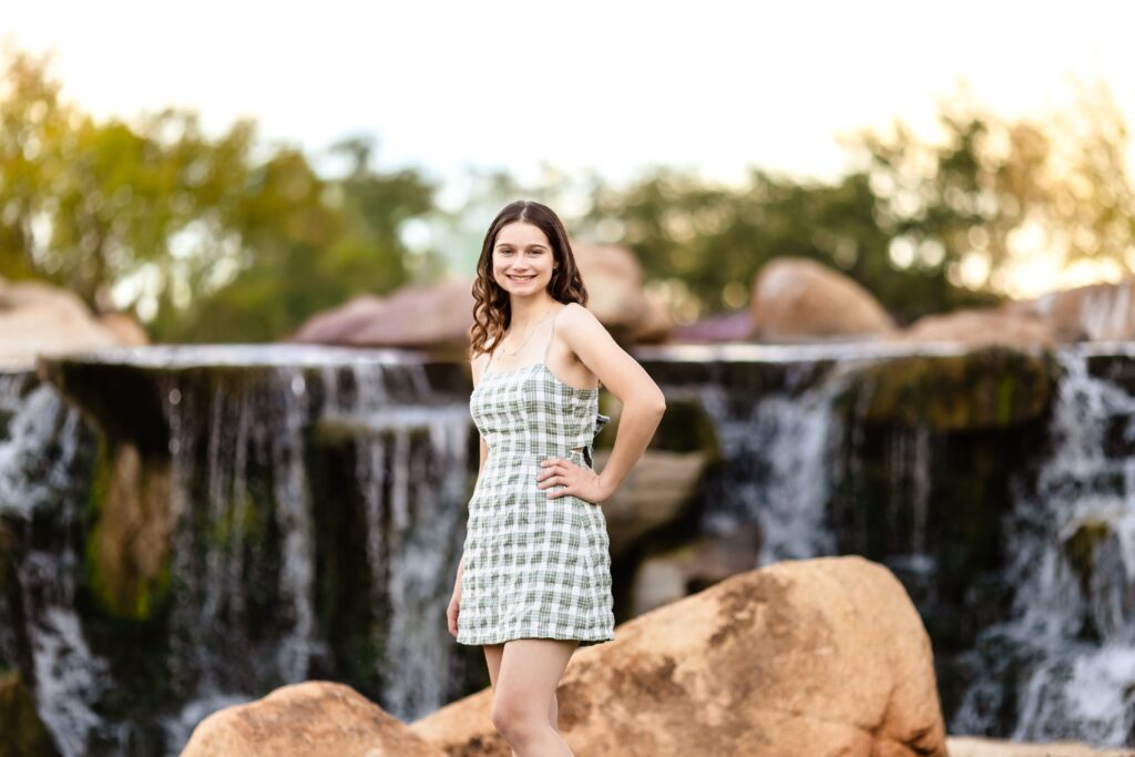 Senior portrait in a green plaid dress beside the waterfall at Anthem Community Park